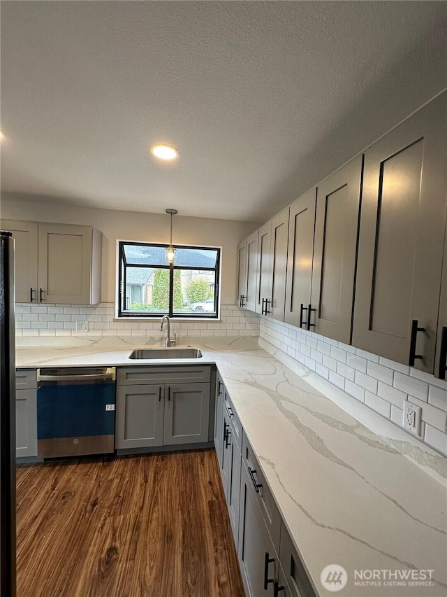 kitchen featuring light stone counters, gray cabinetry, a sink, stainless steel dishwasher, and dark wood-style floors