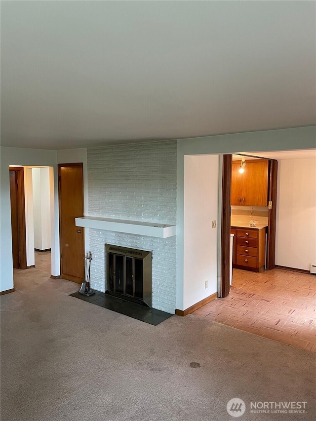 unfurnished living room with a brick fireplace, light carpet, and baseboards