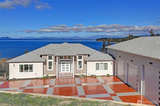 view of front facade featuring a garage, driveway, a water and mountain view, and roof with shingles