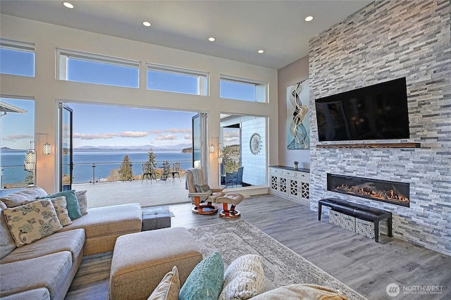 living area featuring recessed lighting, a stone fireplace, wood finished floors, and a towering ceiling