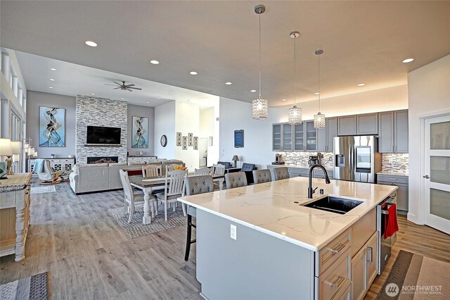 kitchen with light wood-type flooring, a sink, stainless steel refrigerator with ice dispenser, a kitchen bar, and tasteful backsplash