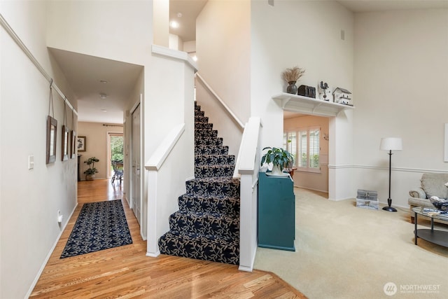 stairs featuring a high ceiling, a healthy amount of sunlight, and wood finished floors