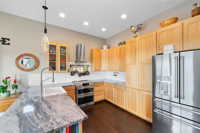 kitchen with light brown cabinets, a peninsula, a sink, appliances with stainless steel finishes, and wall chimney exhaust hood