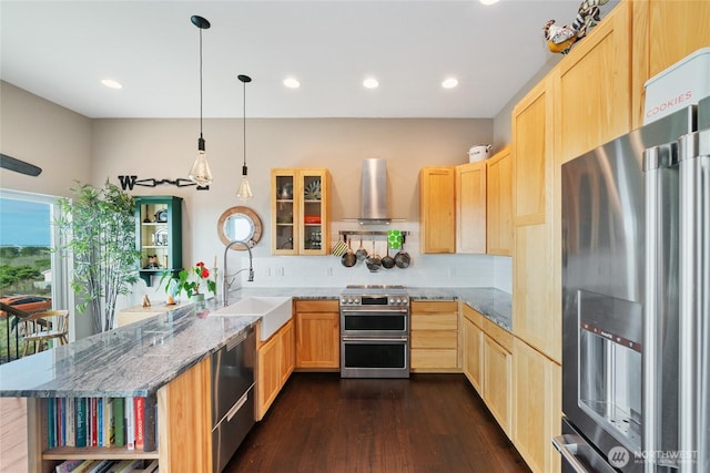 kitchen featuring wall chimney exhaust hood, a peninsula, stainless steel appliances, light brown cabinetry, and a sink