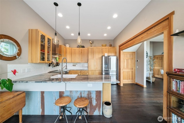 kitchen with high quality fridge, glass insert cabinets, a peninsula, light stone countertops, and a sink