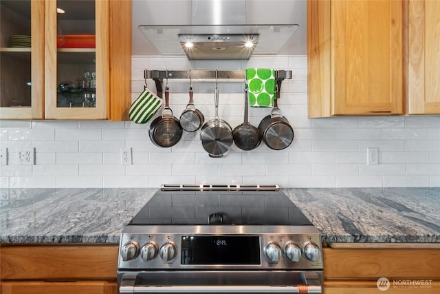 kitchen with decorative backsplash, glass insert cabinets, dark stone countertops, stainless steel electric stove, and exhaust hood