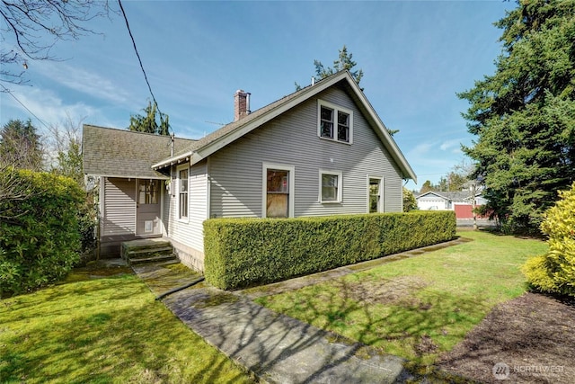 exterior space with a shingled roof, a chimney, and a lawn