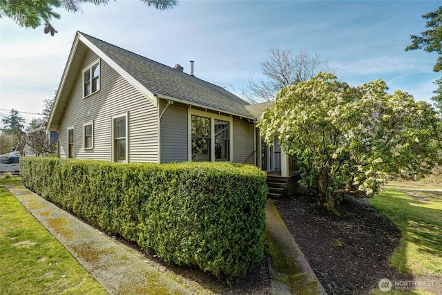 view of home's exterior with a shingled roof, a chimney, and a yard