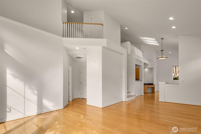 unfurnished living room with baseboards, light wood-type flooring, a towering ceiling, and recessed lighting