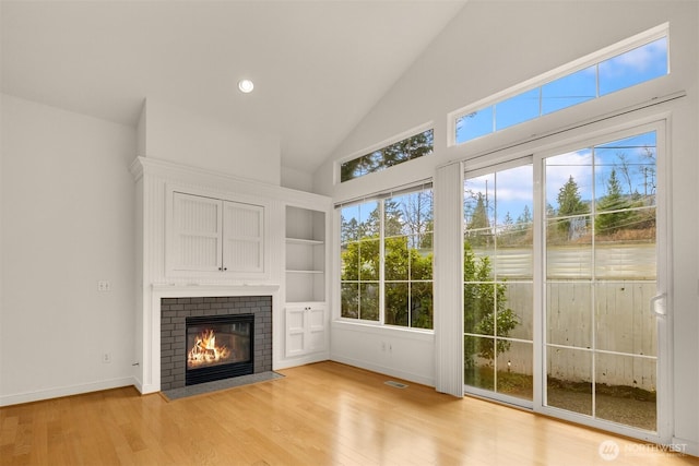 unfurnished living room featuring light wood finished floors, baseboards, visible vents, a fireplace, and high vaulted ceiling