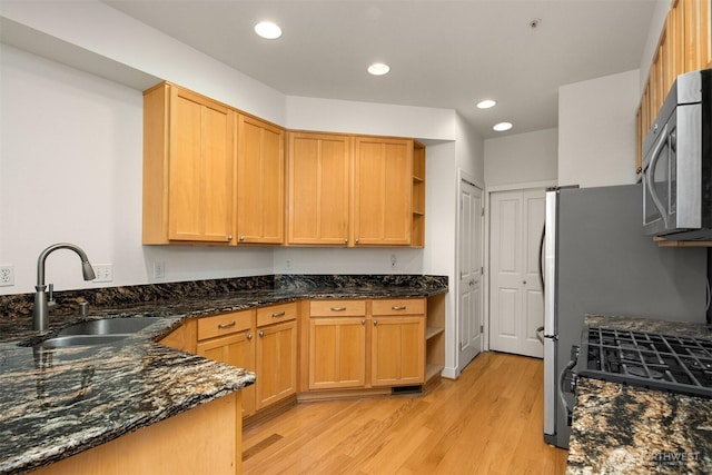 kitchen with dark stone countertops, stainless steel appliances, light wood-style floors, open shelves, and a sink