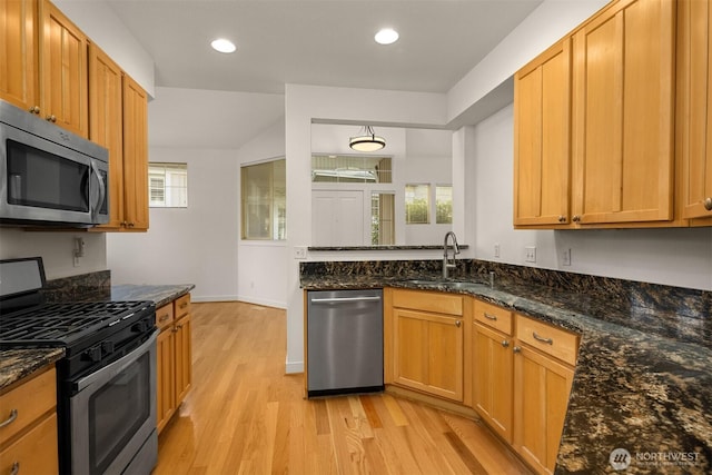 kitchen with light wood-style flooring, dark stone countertops, stainless steel appliances, a sink, and recessed lighting