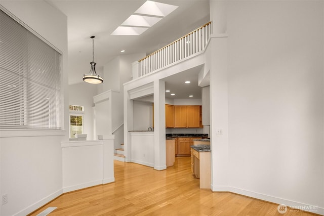 interior space with a skylight, dark countertops, light wood-style flooring, a towering ceiling, and baseboards