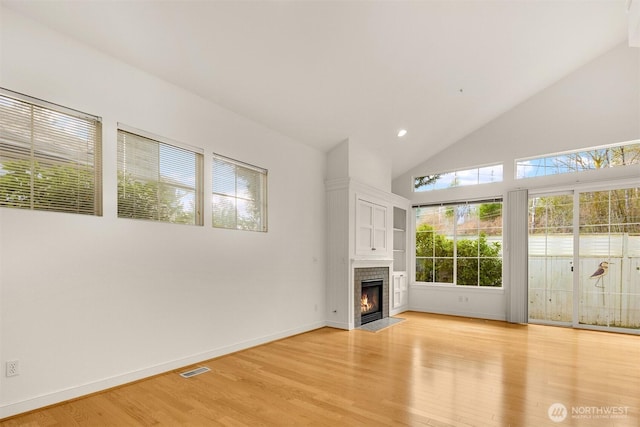 unfurnished living room featuring high vaulted ceiling, a tile fireplace, visible vents, baseboards, and light wood-style floors