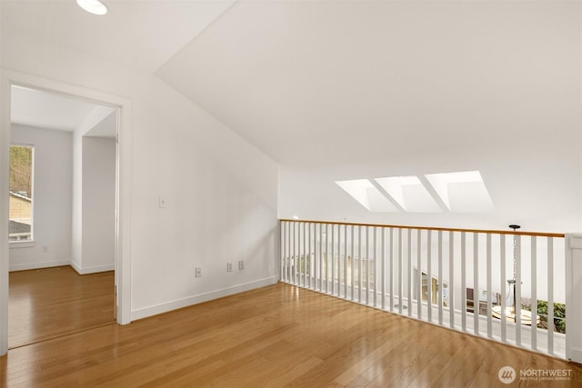 additional living space featuring vaulted ceiling with skylight, baseboards, and wood finished floors