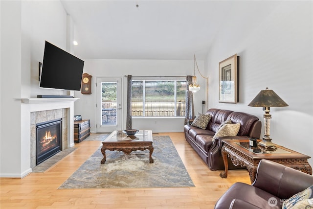 living area featuring high vaulted ceiling, a tiled fireplace, light wood-style floors, a chandelier, and baseboards