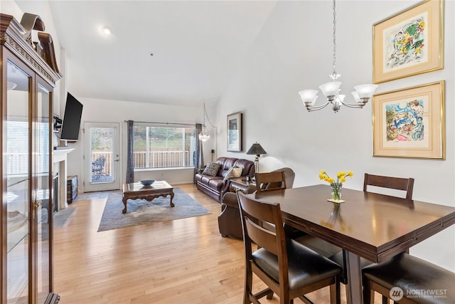 dining space featuring a chandelier, high vaulted ceiling, light wood finished floors, and a fireplace with flush hearth