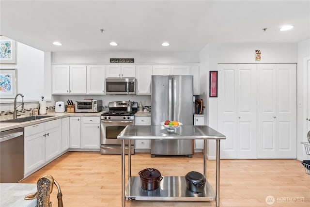 kitchen with stainless steel appliances, light wood-style floors, white cabinetry, and a sink