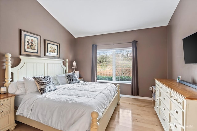 bedroom with baseboards, vaulted ceiling, and light wood finished floors