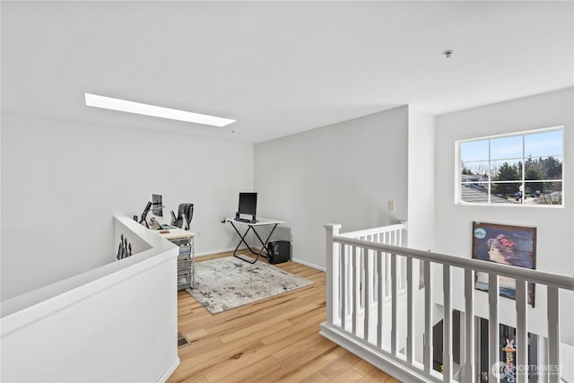 corridor with a skylight, an upstairs landing, and wood finished floors