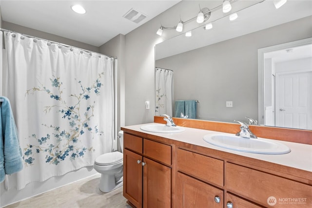 bathroom with toilet, double vanity, a sink, and visible vents