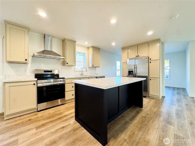 kitchen featuring a kitchen island, wall chimney range hood, light countertops, appliances with stainless steel finishes, and a sink