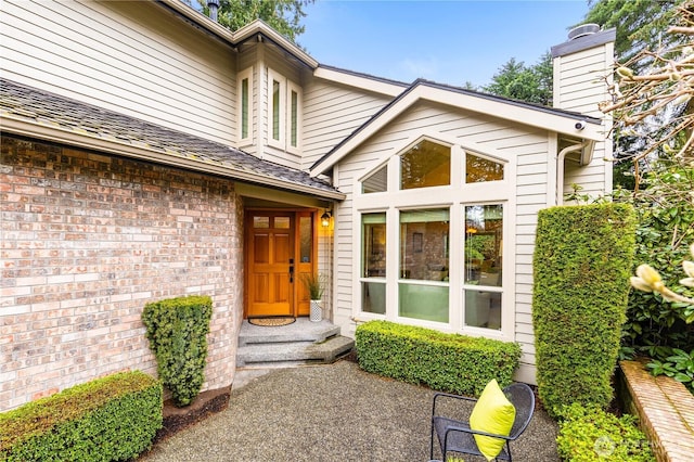 entrance to property with brick siding, a chimney, and roof with shingles