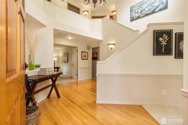 foyer with visible vents, baseboards, stairs, light wood-style flooring, and a towering ceiling