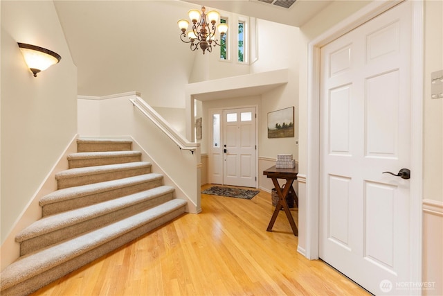 entryway with baseboards, visible vents, stairs, light wood-style floors, and a chandelier