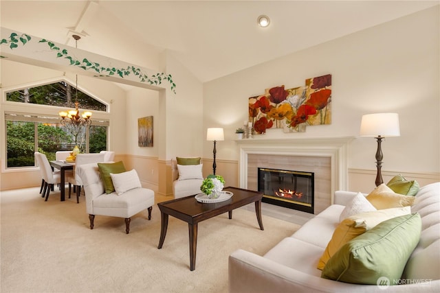 living area featuring a glass covered fireplace, vaulted ceiling, carpet flooring, and an inviting chandelier