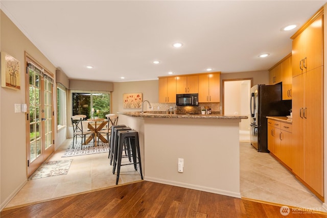 kitchen with a breakfast bar, light wood-style flooring, light stone counters, backsplash, and black microwave