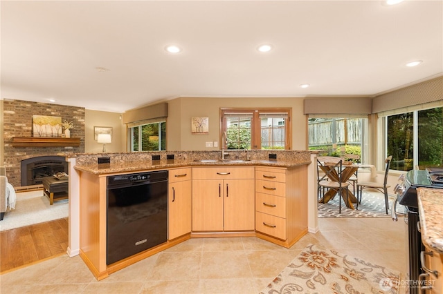 kitchen with light brown cabinets, a sink, black dishwasher, light tile patterned floors, and light stone countertops