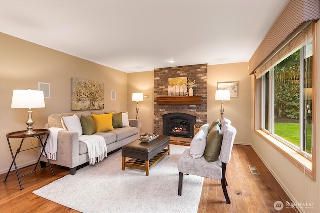 living room featuring visible vents, crown molding, baseboards, a fireplace, and wood finished floors