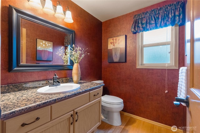 half bathroom with toilet, vanity, baseboards, and wood finished floors