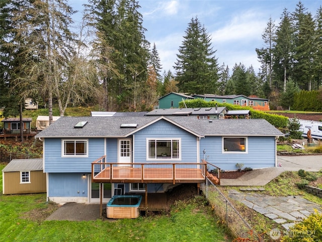 back of house with a hot tub, roof with shingles, a deck, an outdoor structure, and a shed