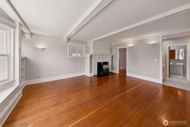 unfurnished living room with hardwood / wood-style flooring, baseboards, and a glass covered fireplace