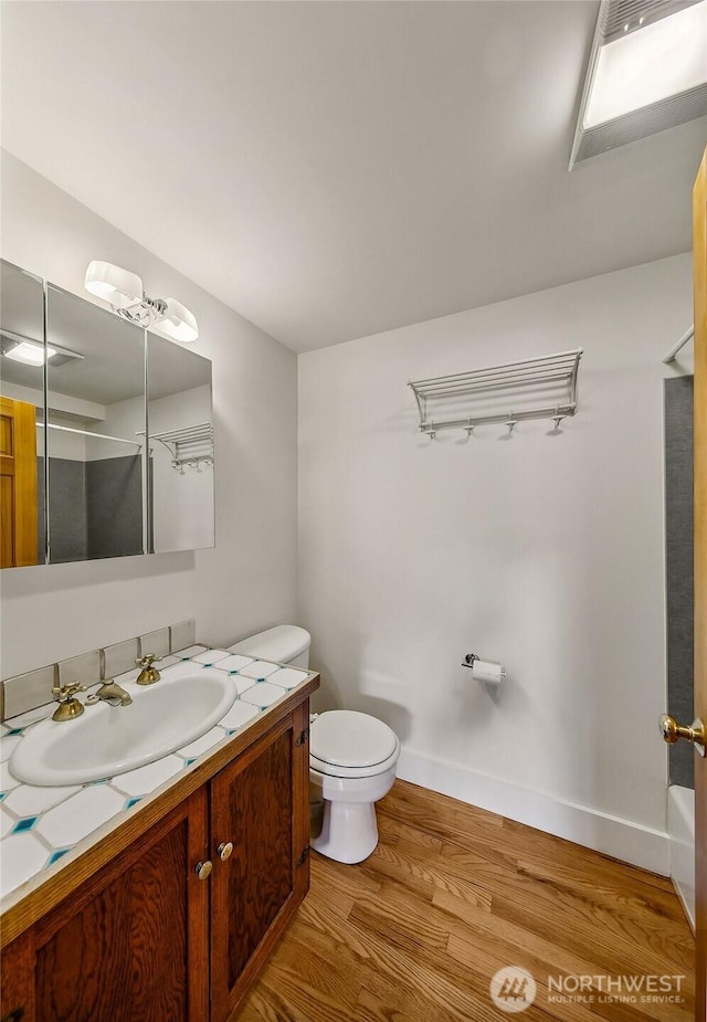 bathroom with baseboards, toilet, wood finished floors, walk in shower, and vanity