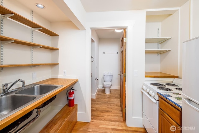 kitchen featuring open shelves, light countertops, light wood-style flooring, a sink, and white appliances