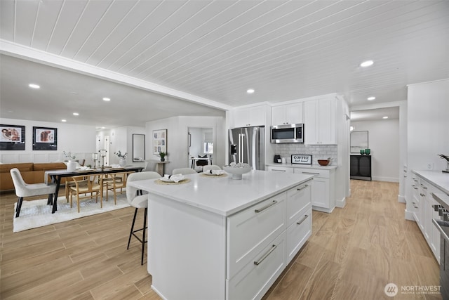 kitchen featuring stainless steel appliances, white cabinetry, light wood-style floors, and a breakfast bar area