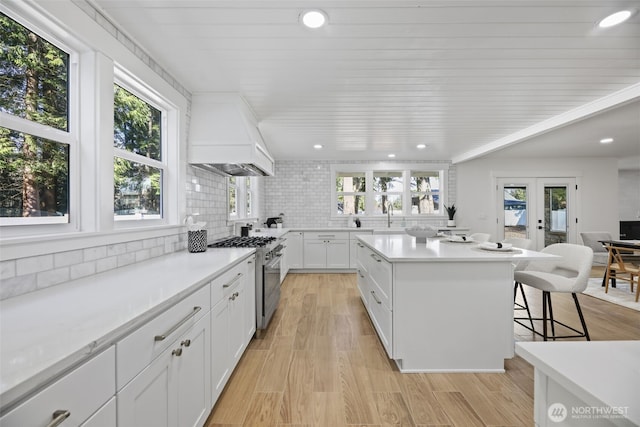 kitchen with tasteful backsplash, custom range hood, stainless steel stove, french doors, and a kitchen bar