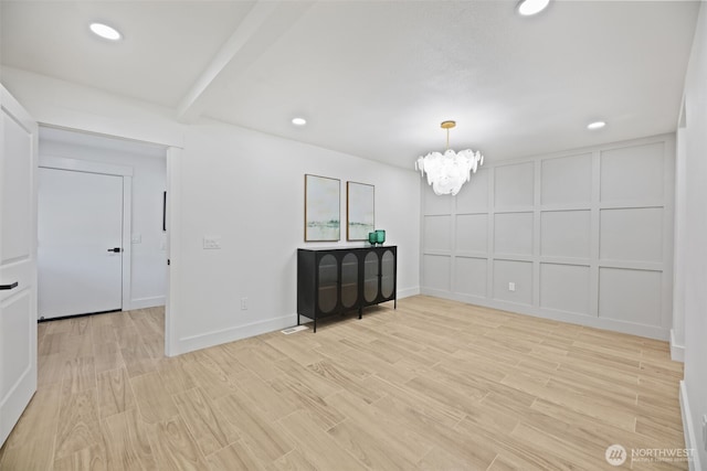 unfurnished room with a chandelier, light wood-style floors, recessed lighting, and a decorative wall