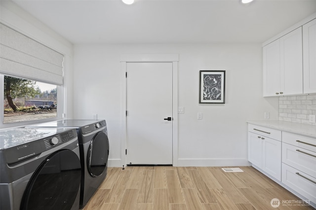 laundry area featuring visible vents, baseboards, light wood-type flooring, cabinet space, and washer and clothes dryer