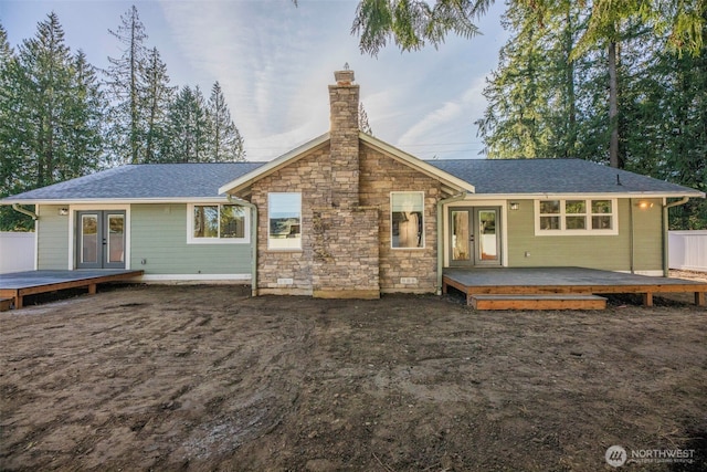 rear view of house featuring french doors, a chimney, a shingled roof, stone siding, and a wooden deck