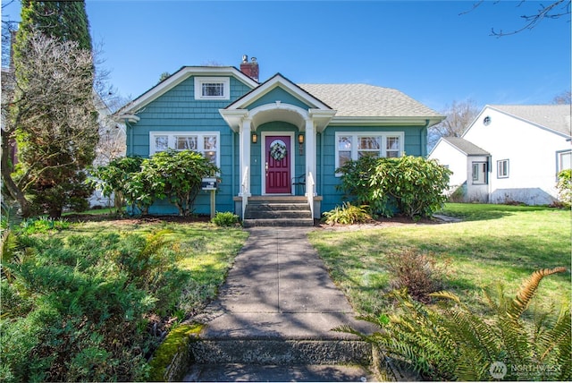 bungalow-style home featuring a shingled roof, a front yard, and a chimney