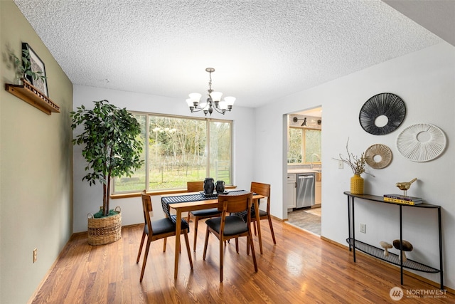 dining space with a notable chandelier, light wood finished floors, and a textured ceiling