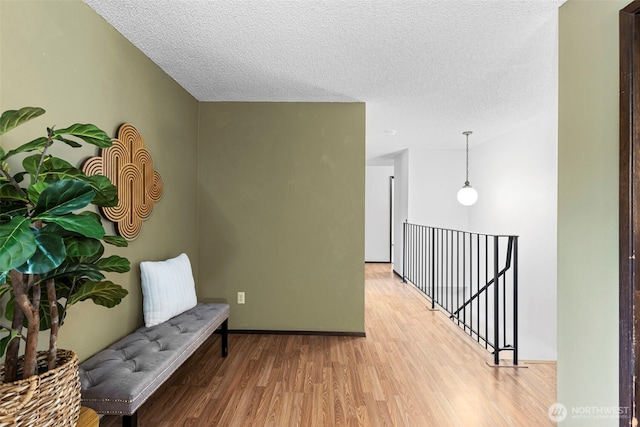 hallway featuring light wood-type flooring, an upstairs landing, and a textured ceiling