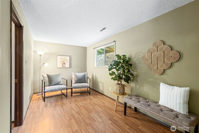 living area with light wood-style floors, visible vents, and a textured ceiling