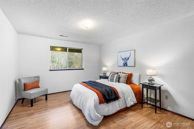 bedroom with visible vents, a textured ceiling, and wood finished floors