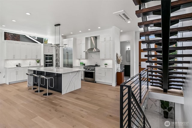 kitchen with premium appliances, visible vents, light wood-style floors, a sink, and wall chimney range hood