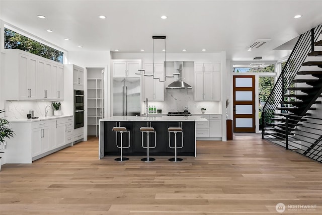 kitchen featuring appliances with stainless steel finishes, a breakfast bar area, plenty of natural light, and wall chimney range hood